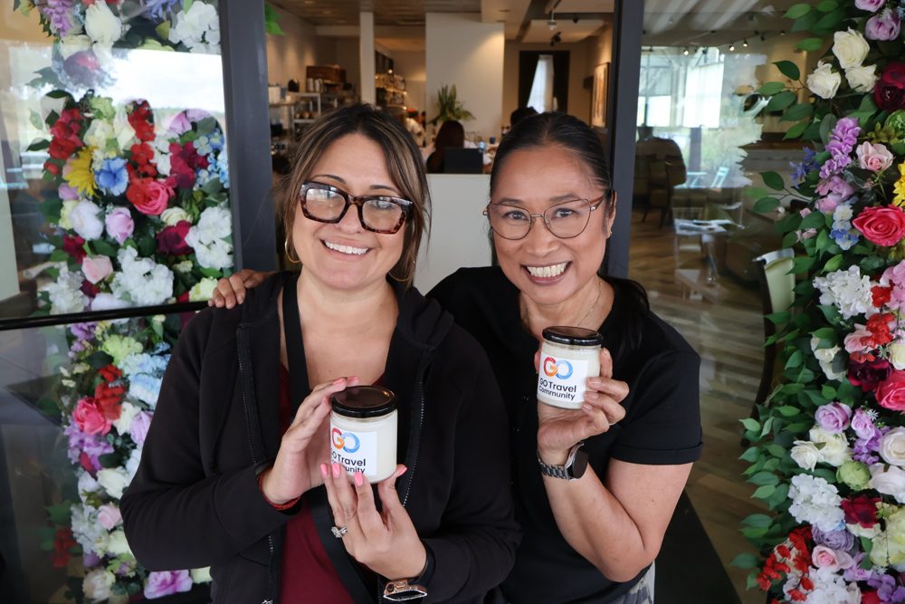 Two smiling community members holding Go Travel Community candles in front of a flower wall